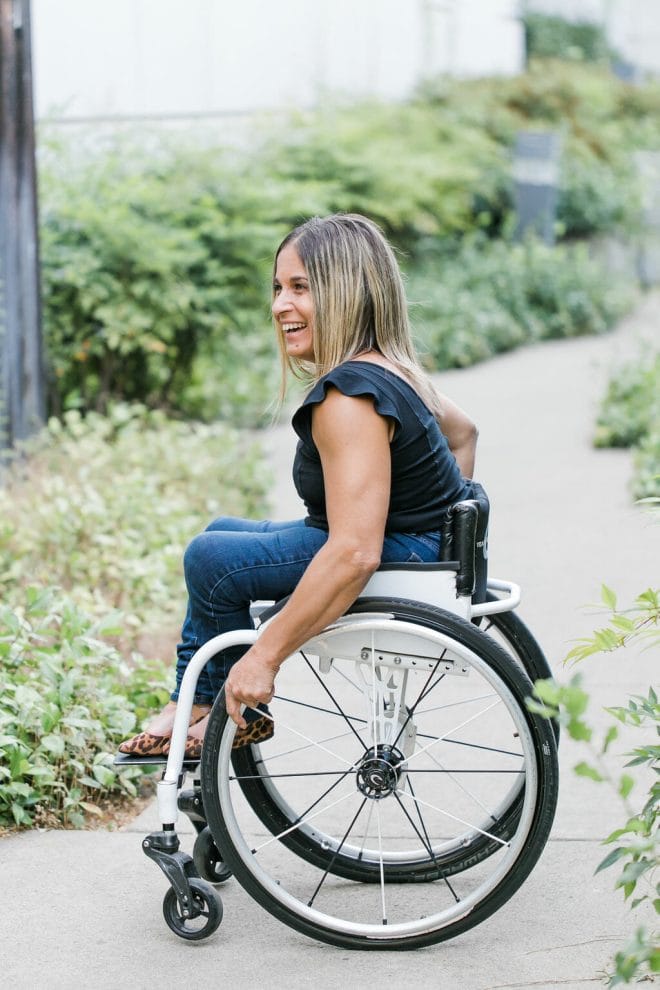 alycia in her wheelchair on a path with foliage on both sides smiling