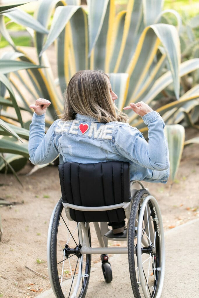 alycia pointing at her back wearing a jean jacket that has patches saying see heart me