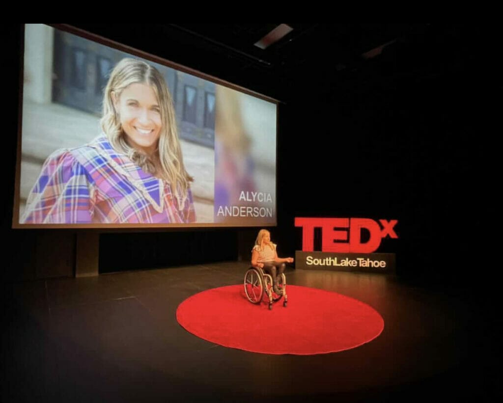 alycia on big red dot with picture of her on big screen behind her along the tedx south lake tahoe sign rehearsing