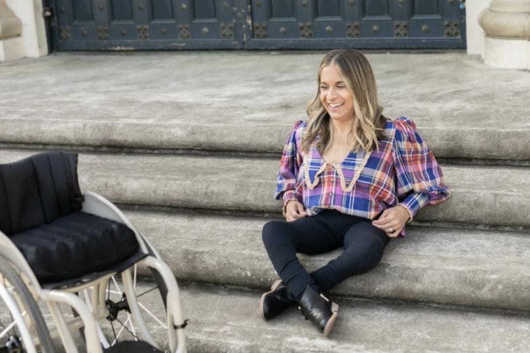 alycia sitting on steps smiling and looking at her wheelchair