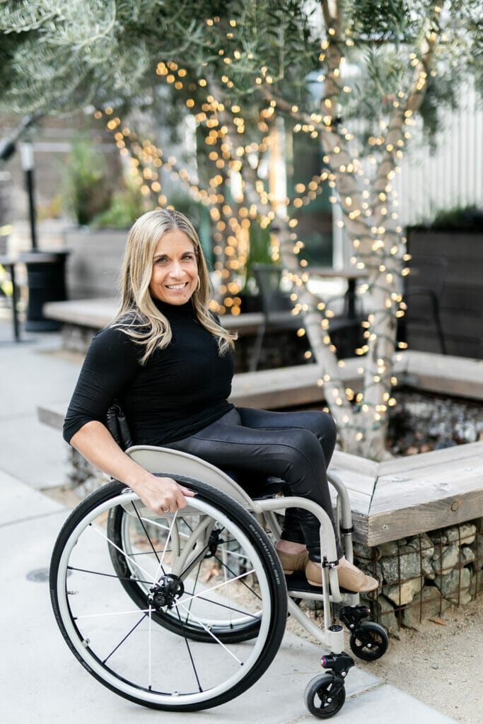 alycia sitting in her wheelchair in front of trees wrapped with lights