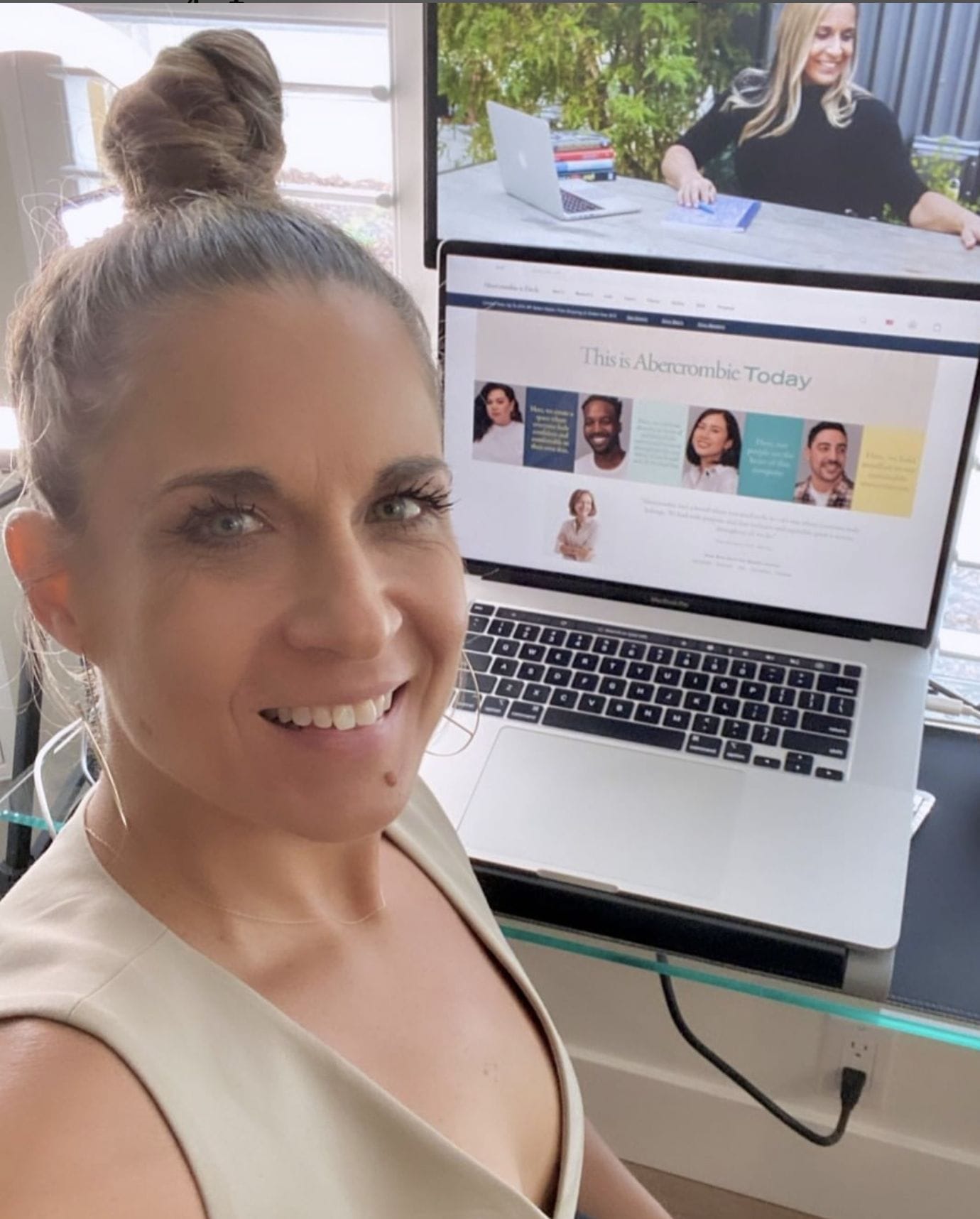 Alycia sitting in studio giving virtual speech to A&F Co team. She is smiling and wearing a tan vest with hair in a high bun.