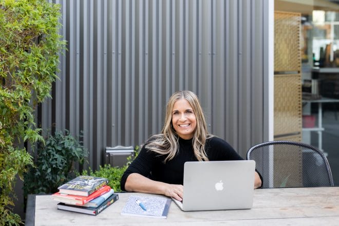 alycia smiling sitting at a table with her books and laptop outside with plants