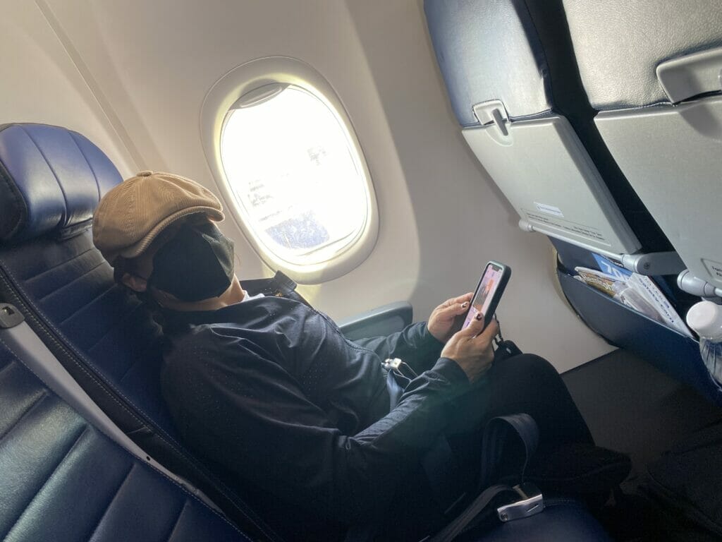 alycia sitting in airplane with a mask on holding her cellphone