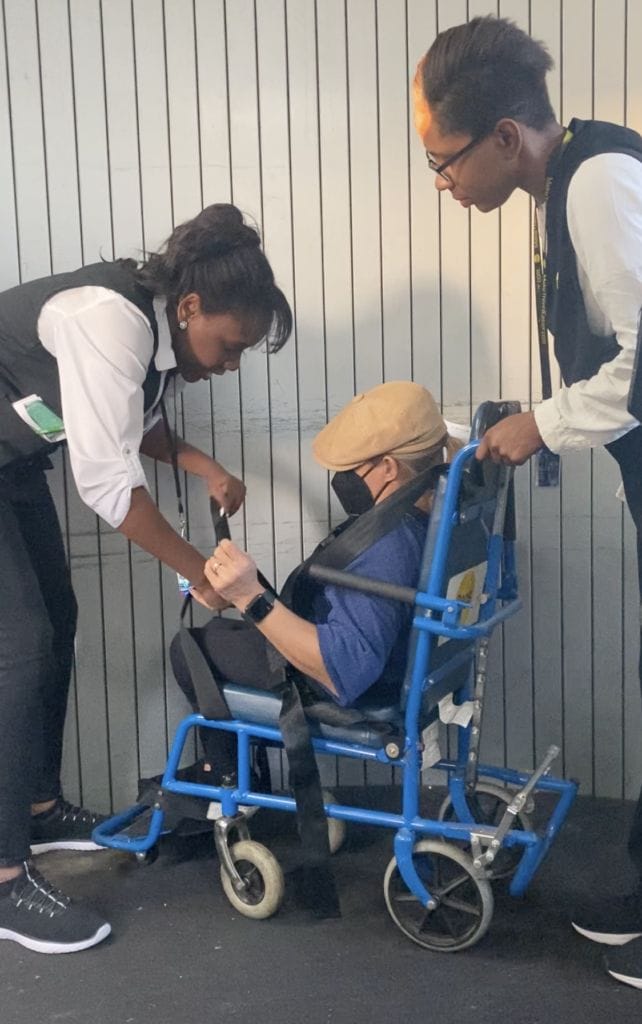 alycia being strapped into aisle chair by airport staff before boarding a plane