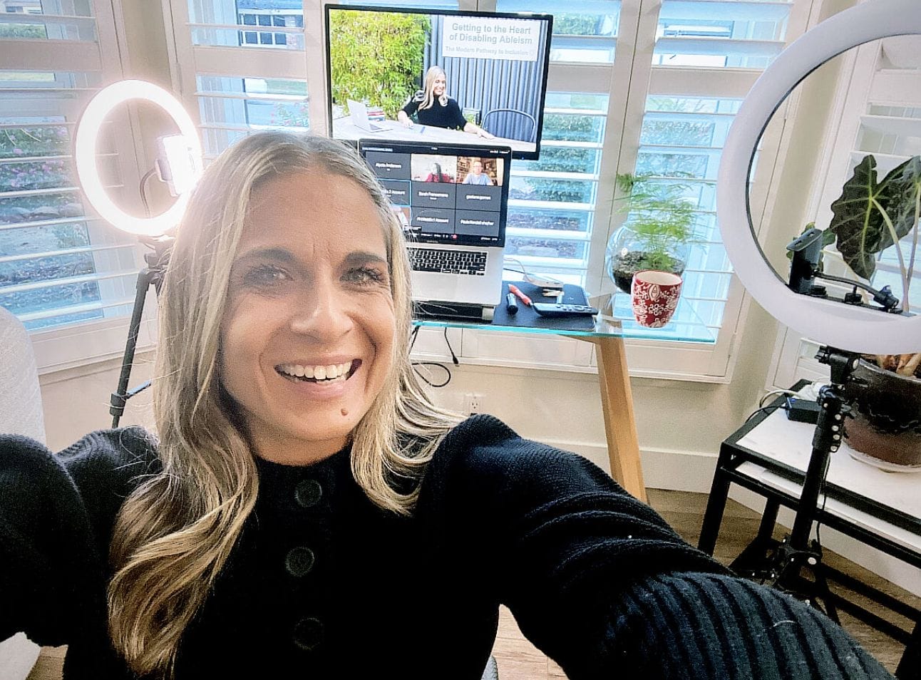 ID: Alycia sitting ready to speak in her studio wearing black and smiling big excited to be at the event!