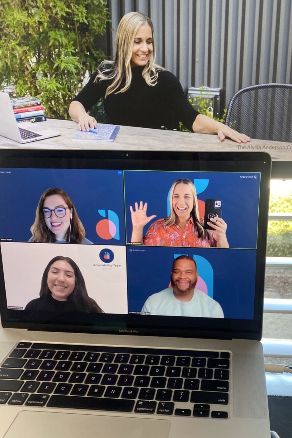 ID: Alycia waving with Confluent AccessAbility Team on a zoom presentation blue screen getting ready to give her #DisablingAbleism#Keynote to the Team. We are all smiling and excited!