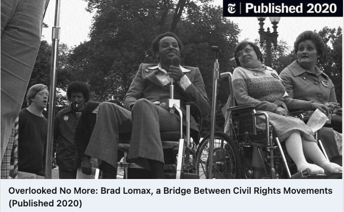 ID: Brad Lomax with Judith Heumann both disability rights advocates bit sitting in their wheelchairs. Brad holding a microphone speaking to the crowd.