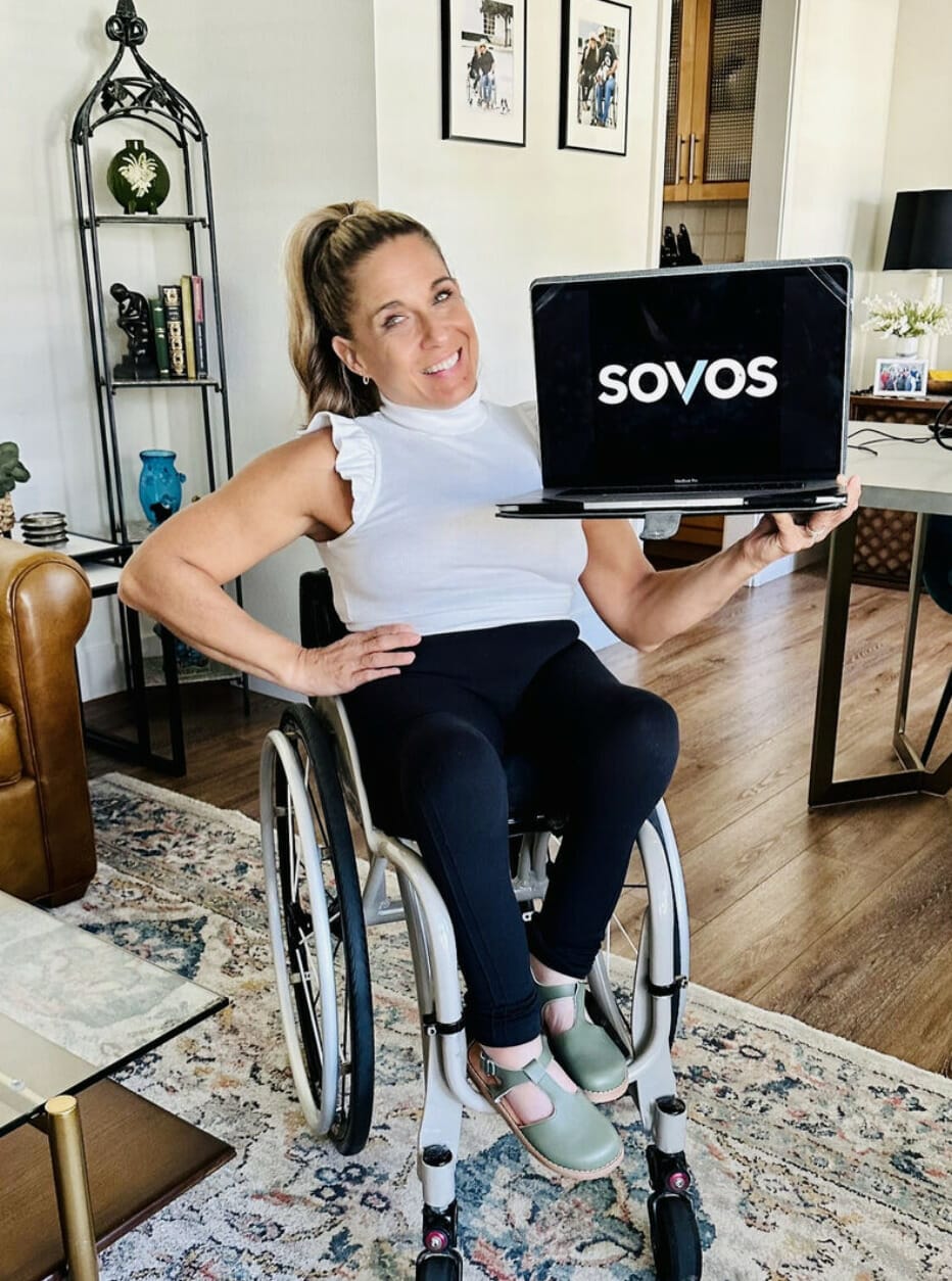 Alycia sitting in wheelchair wearing white and black holding computer after Sovos virtual event!