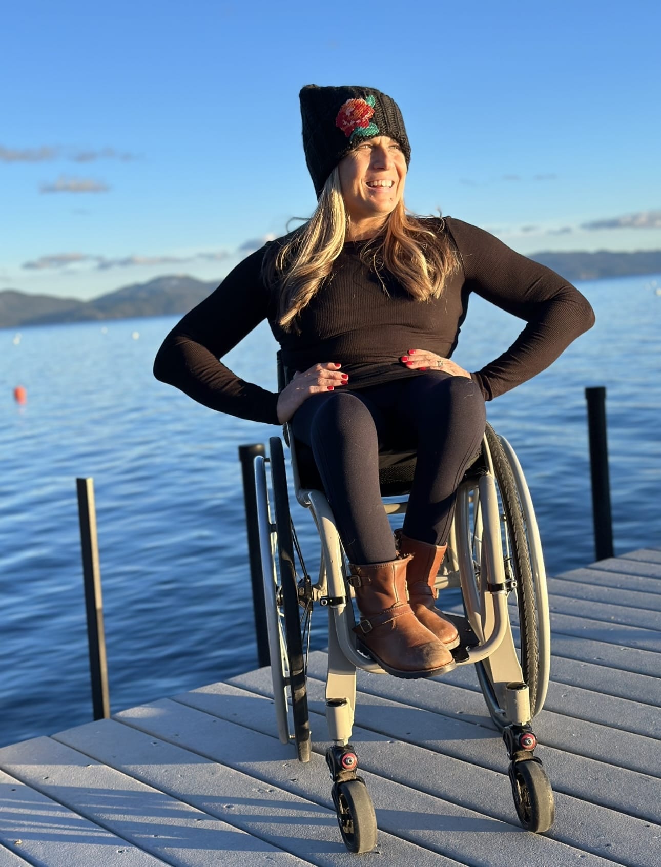 ID: Alycia wearing all black and a beanie with the rose. Sitting on a deck in Lake Tahoe looking over the sunset.