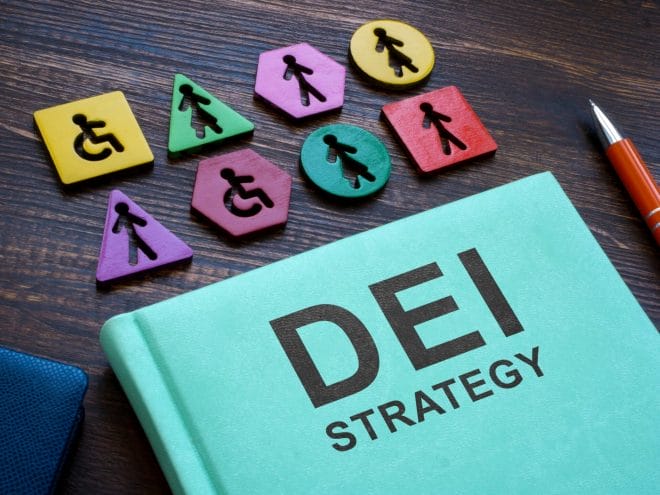 Image of blue book laying on a table that says DEI Strategy with ability symbols above it such as a wheelchair, a woman and a man in varying colors  