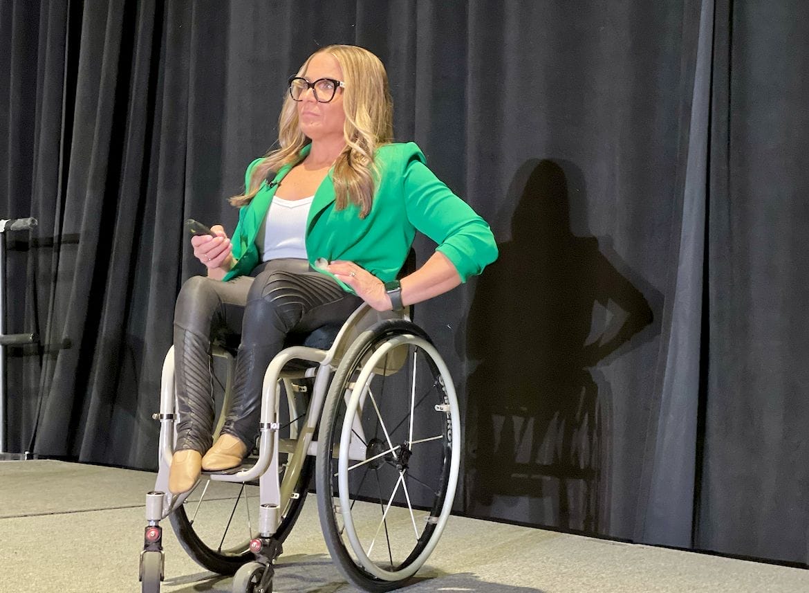 alycia on stage delivering her speech at m t s a conference in a green blazer