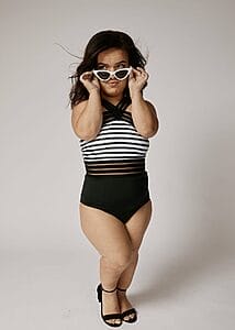 jillian curwin in a swimsuit crossing her legs and holding her sunglasses to her face