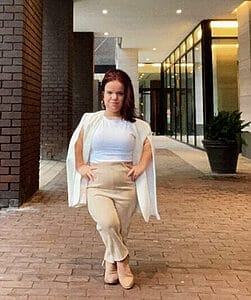 jillian curwin standing on a brick floor wearing tan business attire crossing her legs with her hands in her pockets