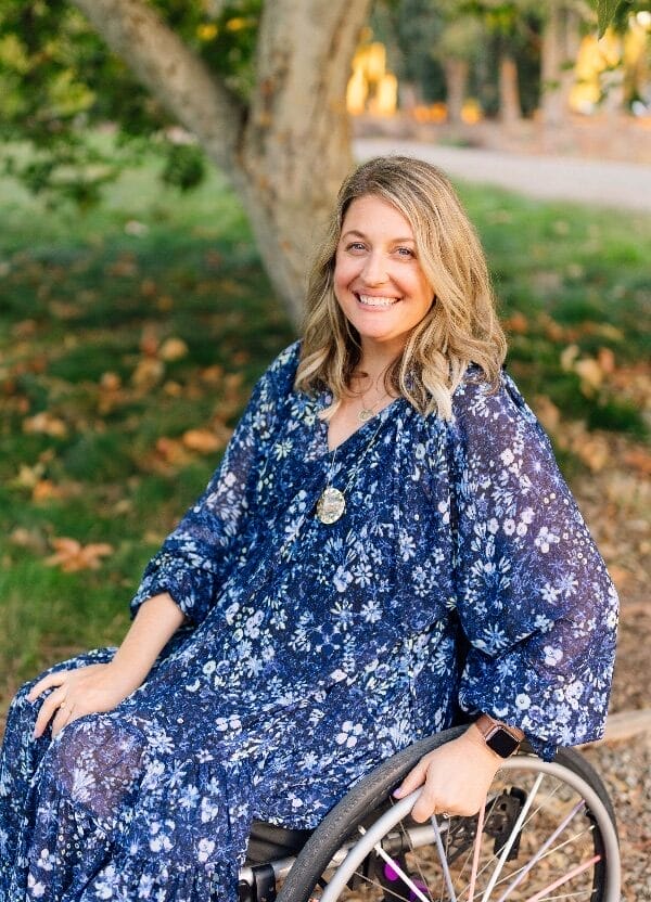 lindsay ulrey sitting in her wheelchair smiling wearing a blue patterned dress