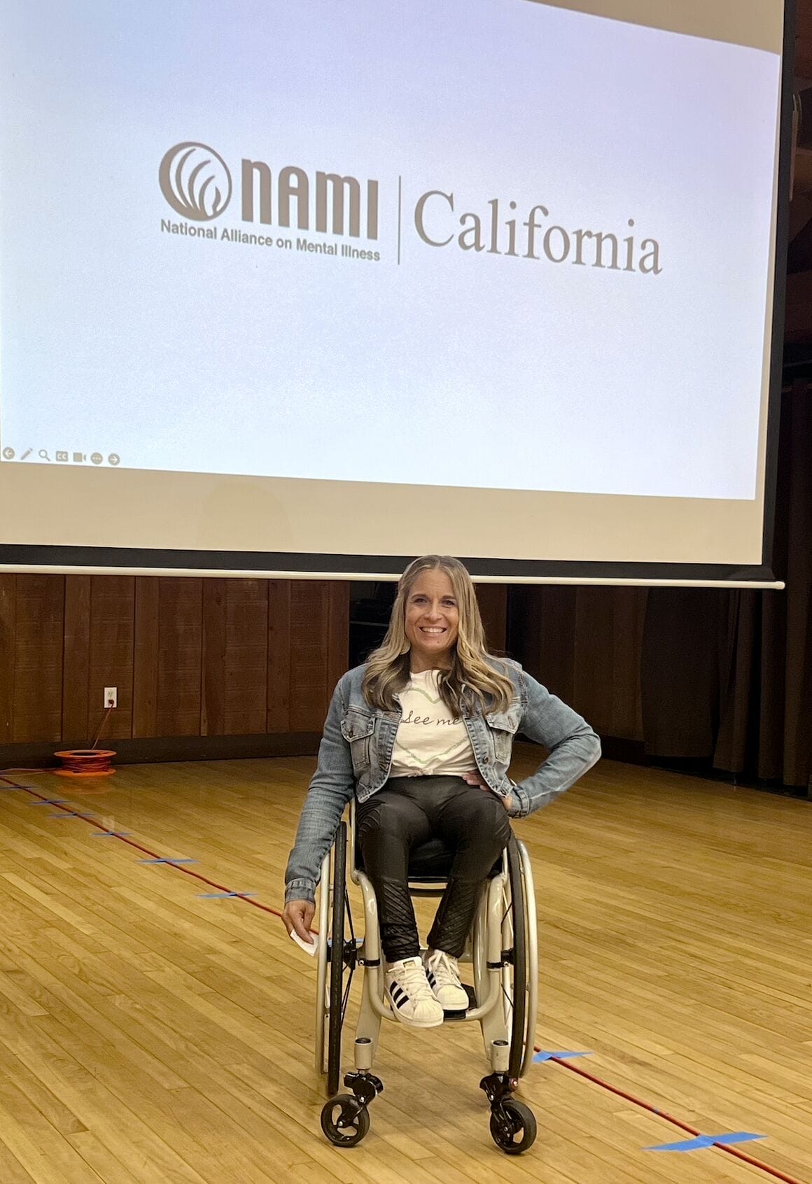 alycia sitting in her wheelchair below a large screen projecting the nami california logo