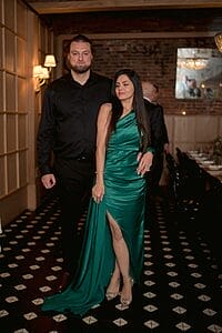 yan vishnepolsky wearing a black formal shirt and trouser standing next to a lady wearing a green shiny long dress