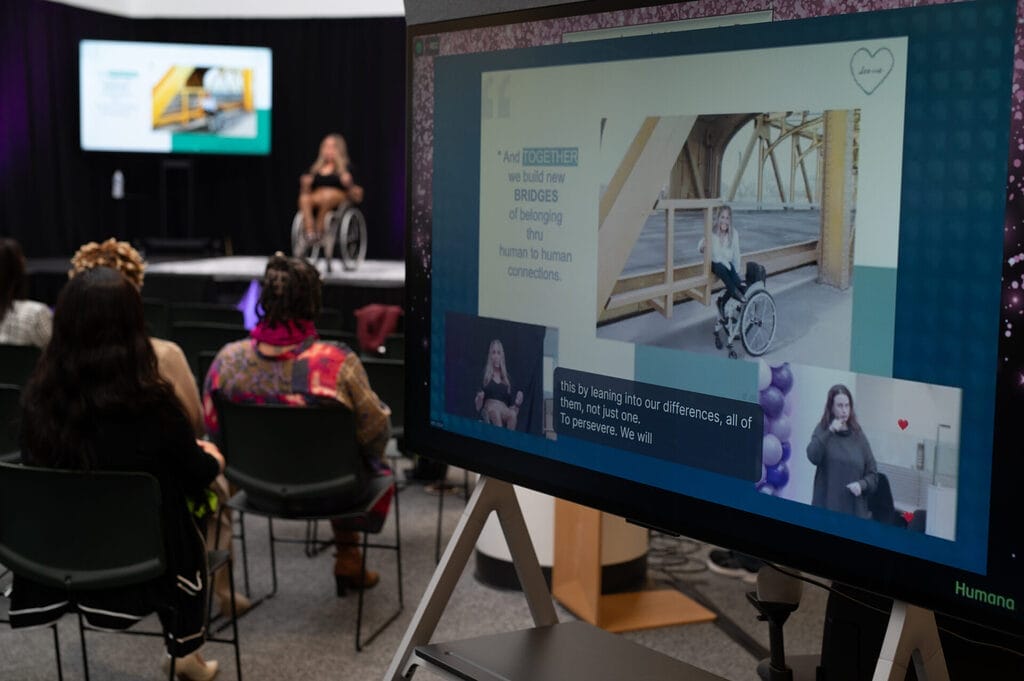image of monitors off stage at live humana event showing a s l signer closed captioning alycia and her slides with alycia on stage in the background