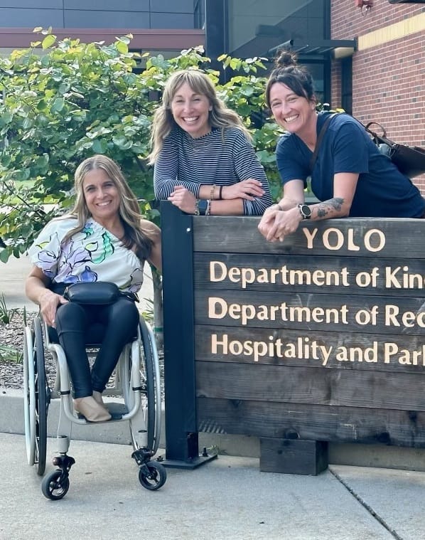 alycia carli and josie sitting next to the yolo hall sign department of kinesiology recreation hospitality and parks management