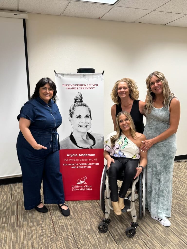 alycia with regina rhiannon and rebecca plumb next to a banner of alycia