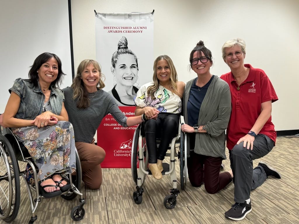 alycia sitting besides kerri and carli josie and doctor rebecca lytle kneeling next to them in front of a banner of alycia