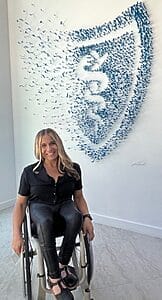 alycia sitting in her wheelchair next to an art piece in the blue shield of california headquarters depicting their logo