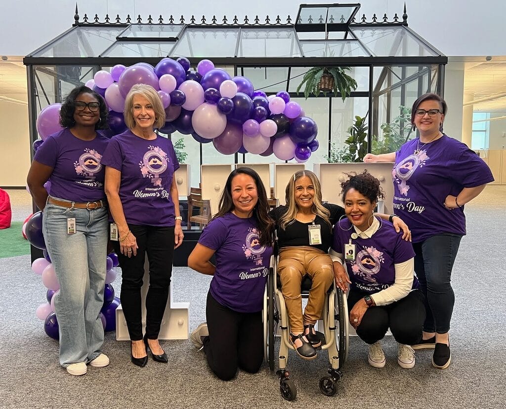 alycia posing with members of the organizing team in front of an i w d sign with purple balloons
