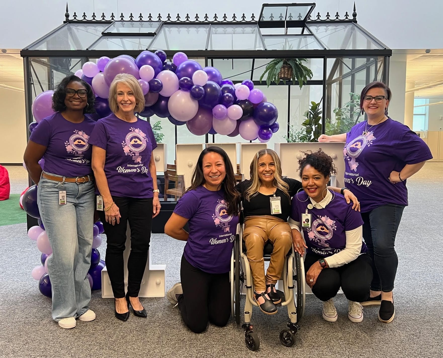 alycia posing with members of the organizing team in front of an i w d sign with purple balloons