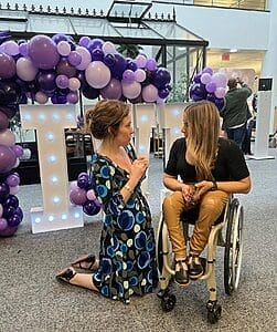 alycia with woman kneeling to talk with alycia in front of the i w d sign with purple balloons
