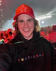 mason branstrator wearing a red baseball hat and black hoodie that says emotional on it smiling with some kind of event crowd behind him