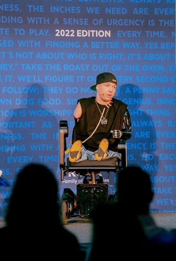ryan hudson peralta sitting on a stage in front of a crowd in his power wheelchair