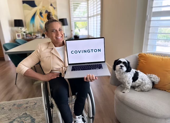 alycia holding er laptop with the covington logo on it sitting next to her on a chair is her dog