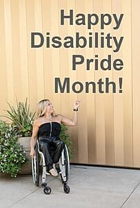 alycia in front of a golden wall pointing up at words that say happy disability pride month