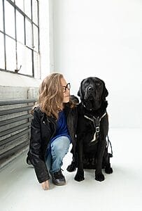 cassidy huff kneeling down with her black labrador inside wearing a leather jacket