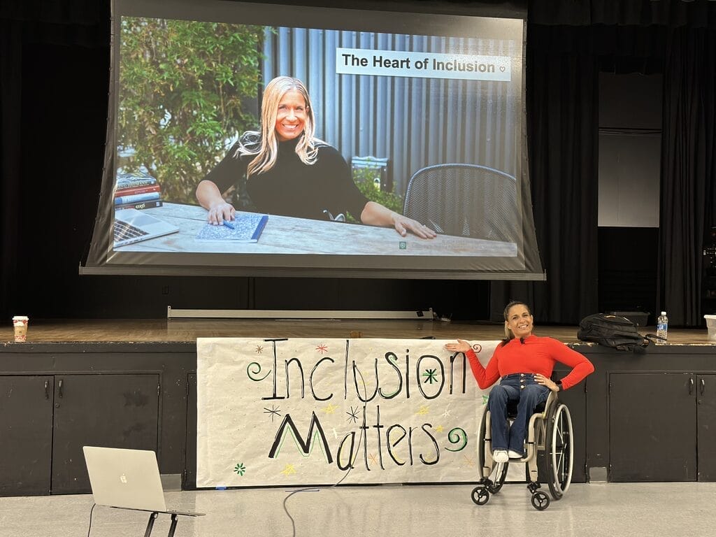 Alycia wearing read speaking to 400 middle school students near and inclusion matters sign