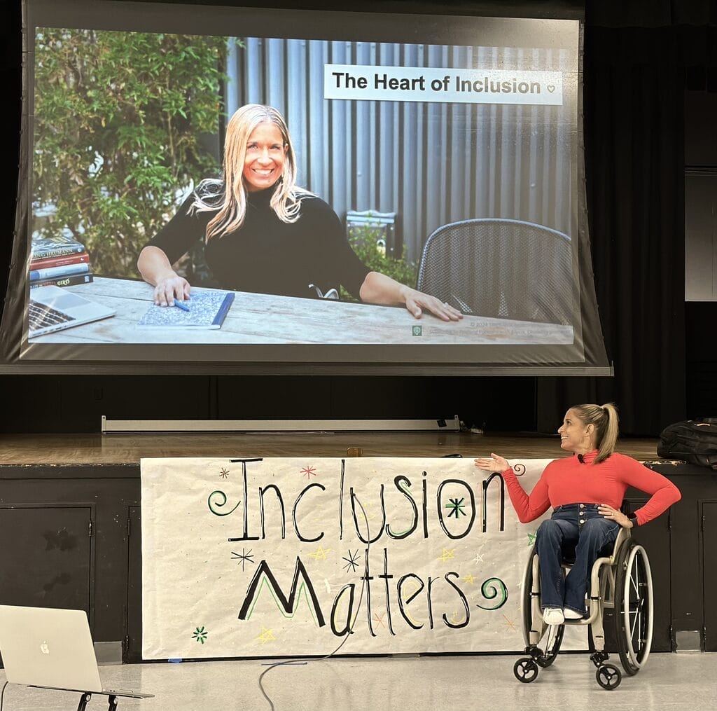Alycia wearing red sitting in wheelchair near a sign that says inclusion matters