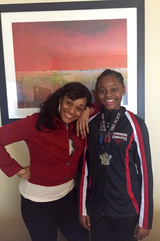 nevaeh standing next to her mom wearing her gymnastics outfit and a medal around her neck