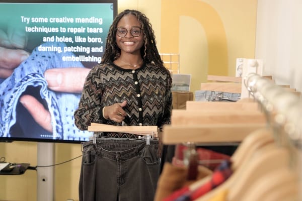 nevaeh holding clothes on a hangar in front of a tv display and clothes rack