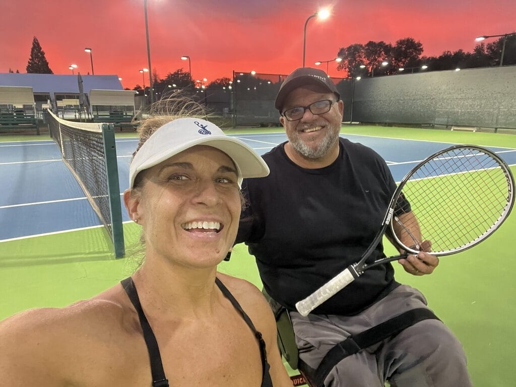 marty and alycia sitting on a tennis court with a magnificent orange sunset behind them