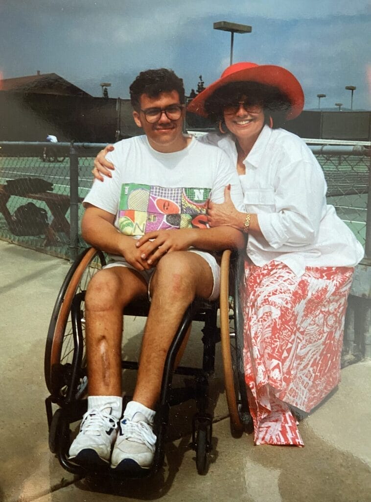 marty sitting in his tennis wheelchair with his mom kneeling and hugging him