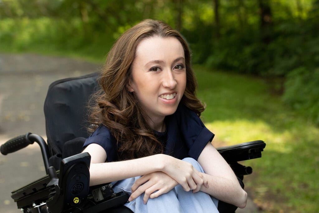 avery roberts sitting in her wheelchair crossing her arms she is wearing blue jeans and a black tee