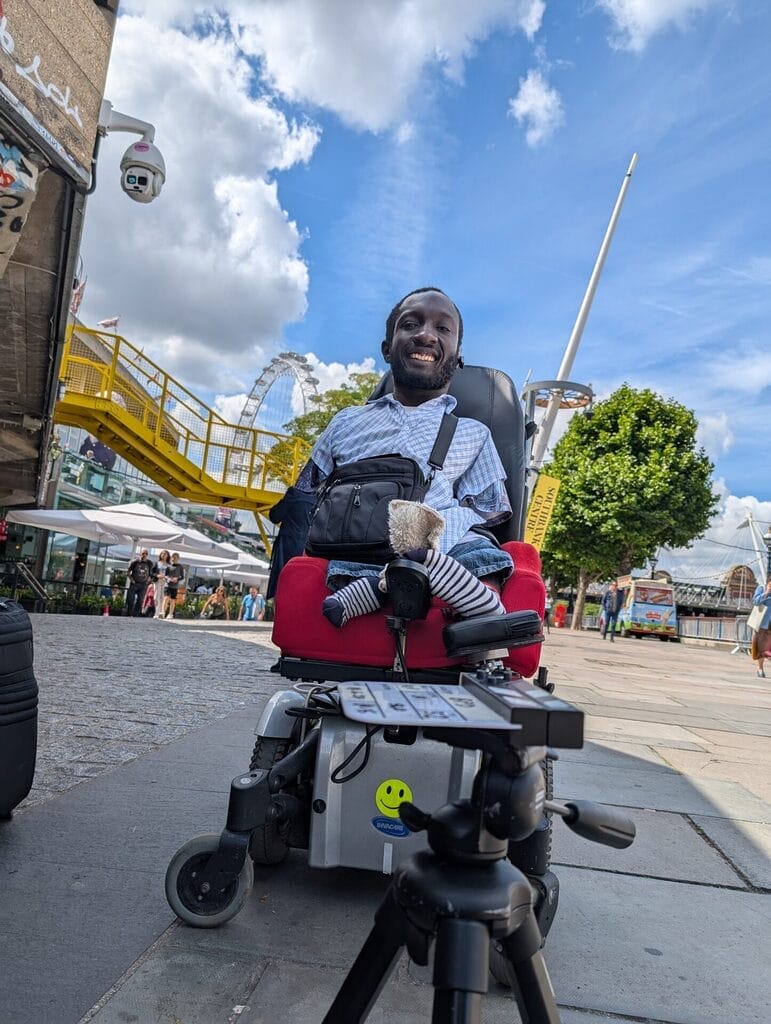 isaac harvey sitting in hiw wheelchair with a camera stand in front of him on the ground