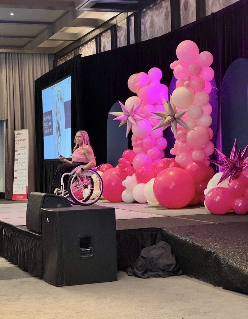 Alycia speaking on stage with pink balloons behind her
