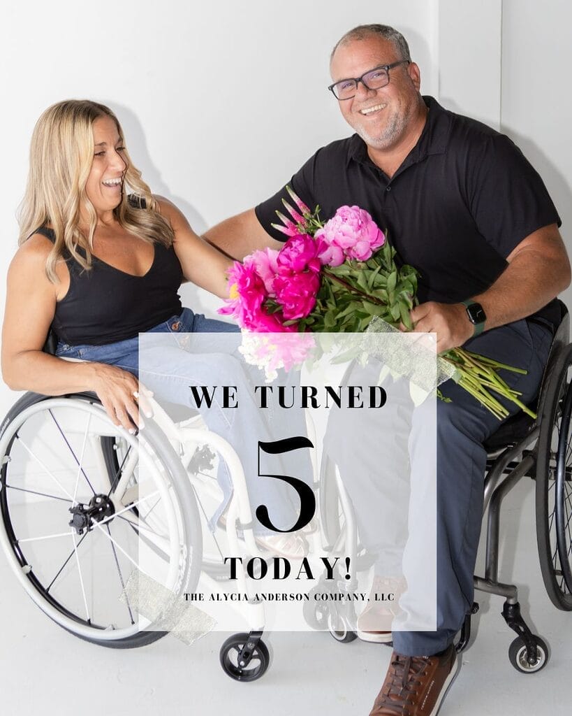 Alycia and Marty, both in wheelchairs, smiling and laughing in a bright white studio. Alycia reaches toward Marty as he holds a bouquet of bright pink flowers. Overlay text: “We turned 5 today! The Alycia Anderson Company, LLC.”