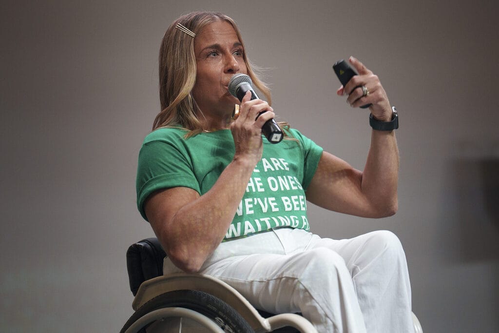 Alycia speaking on stage in her wheelchair, mic in hand, wearing a green shirt: “We are the ones we’ve been waiting for!”