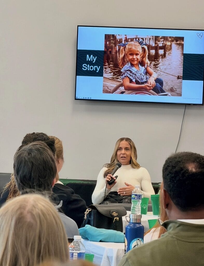 alycia speaking at the special olympics virginia fitness collaborative in holding a microphone under her my story slide on the wall behind her