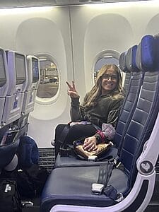 alycia sitting on an airplane smiling and giving the peace sign