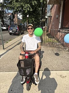 james ian in a scooter with balloons tied to it on city streets