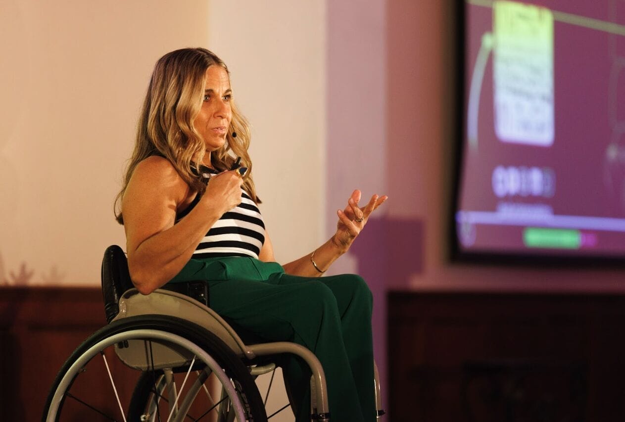 Alycia Anderson speaking on stage in her wheelchair, gesturing while delivering her keynote.