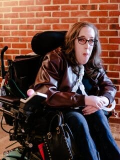 peri finkelstein sitting in her powerchair in front of a brick wall